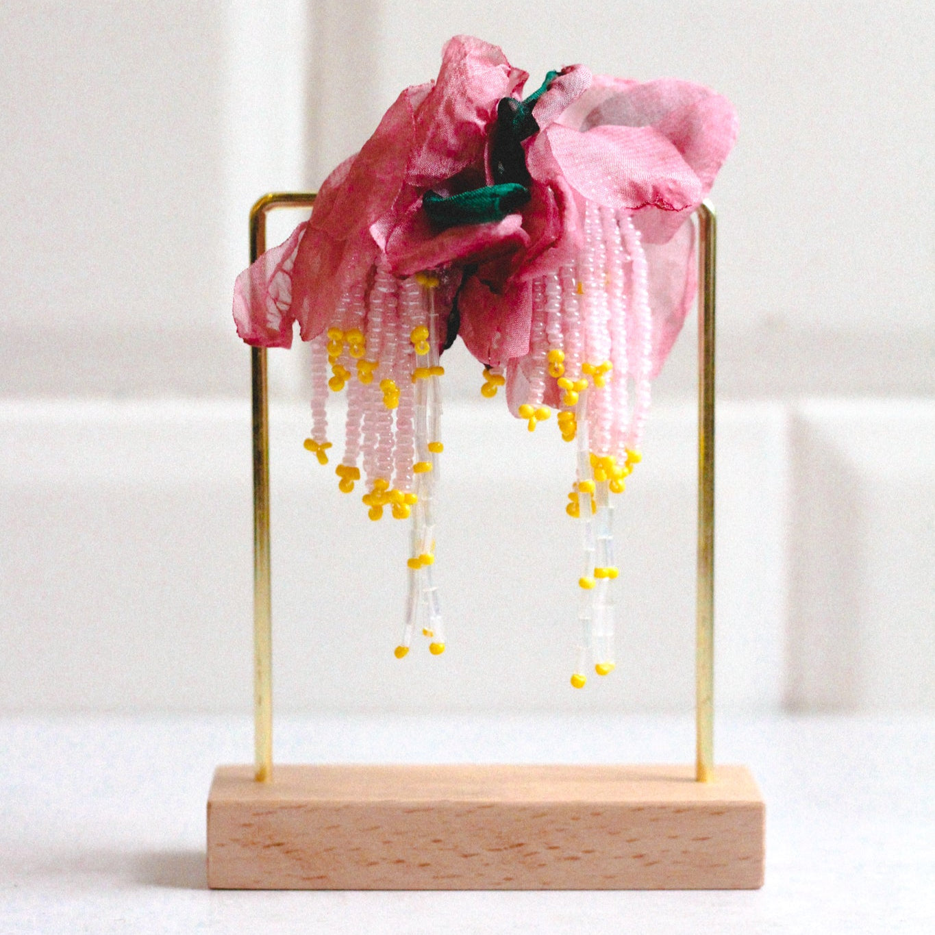 A pair of dusty pink floral earrings displayed on a stand against a white background.