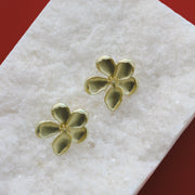 Gold four-leaf clover earrings on a white cloth with a red background