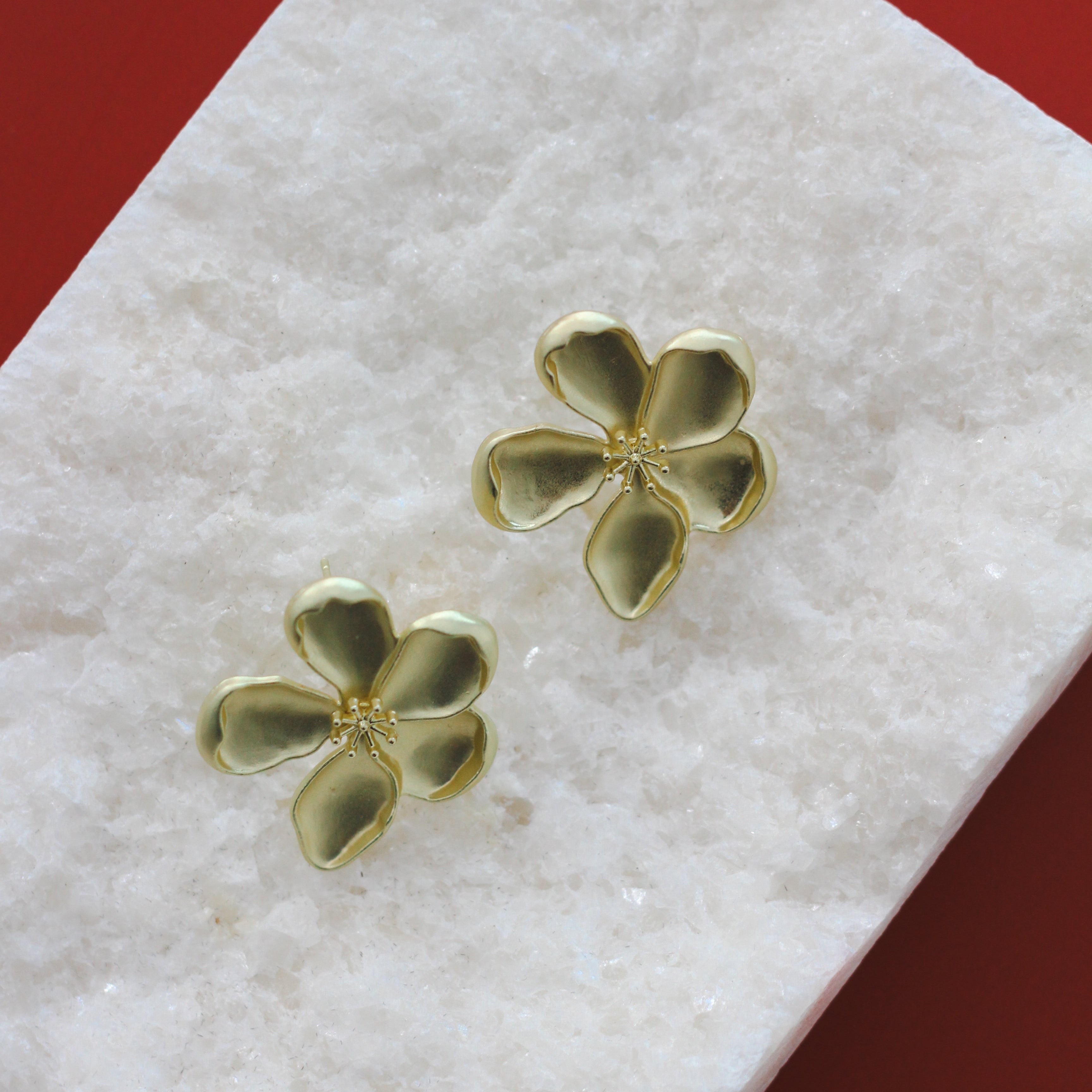 Gold four-leaf clover earrings on a white cloth with a red background